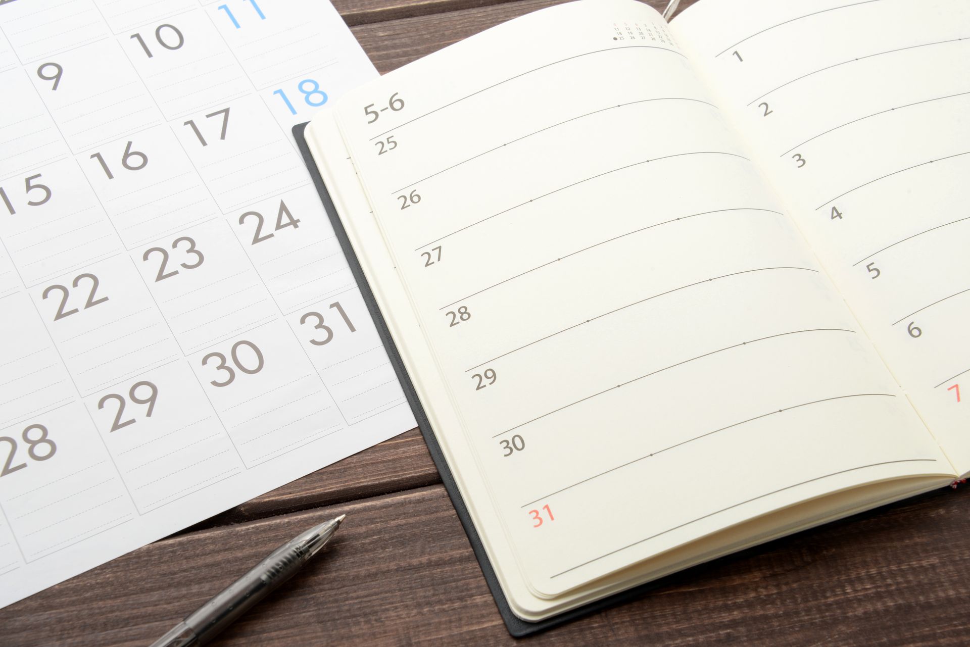 Un agenda ouvert à côté d'un calendrier mensuel avec un stylo sur un bureau en bois