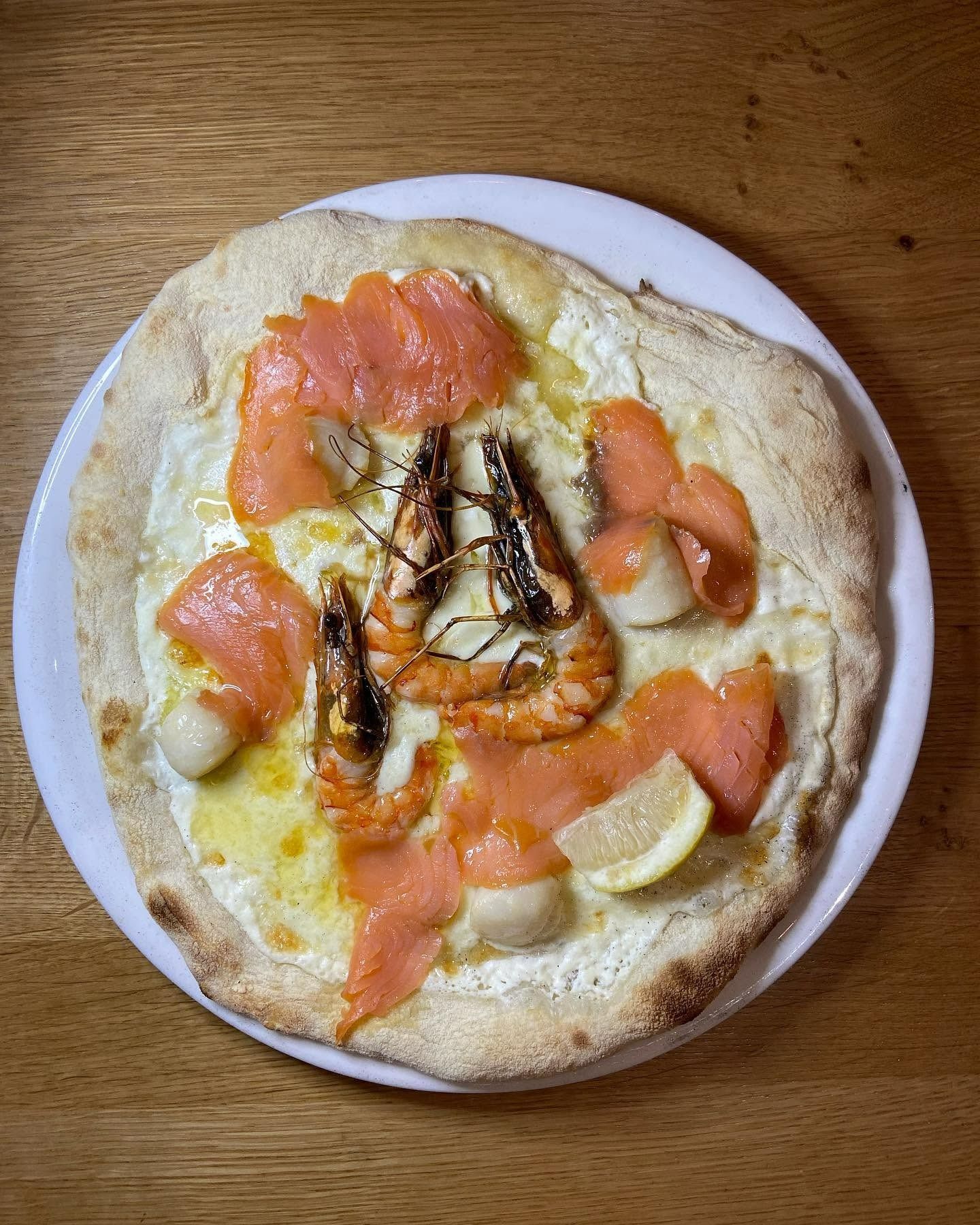 Pizza maison au saumon, crevettes, quartiers de citron et fromage fondu sur une assiette blanche