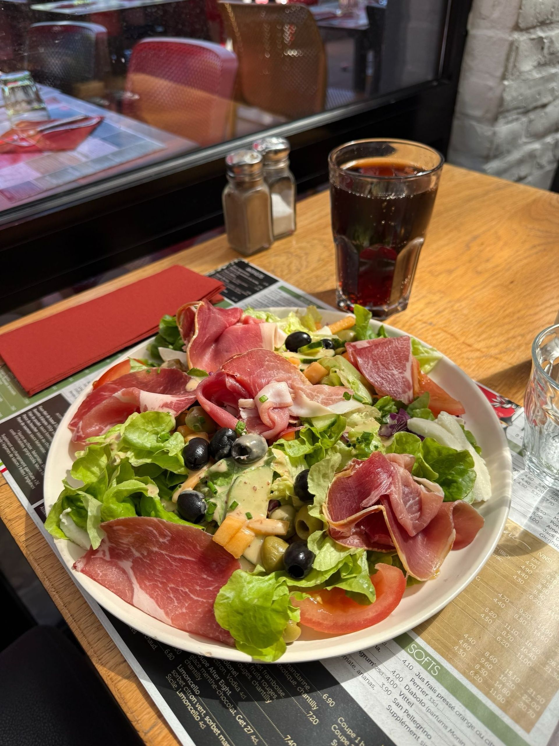 Salade italienne au prosciutto sur une table de restaurant, accompagnée d'un verre de soda brun