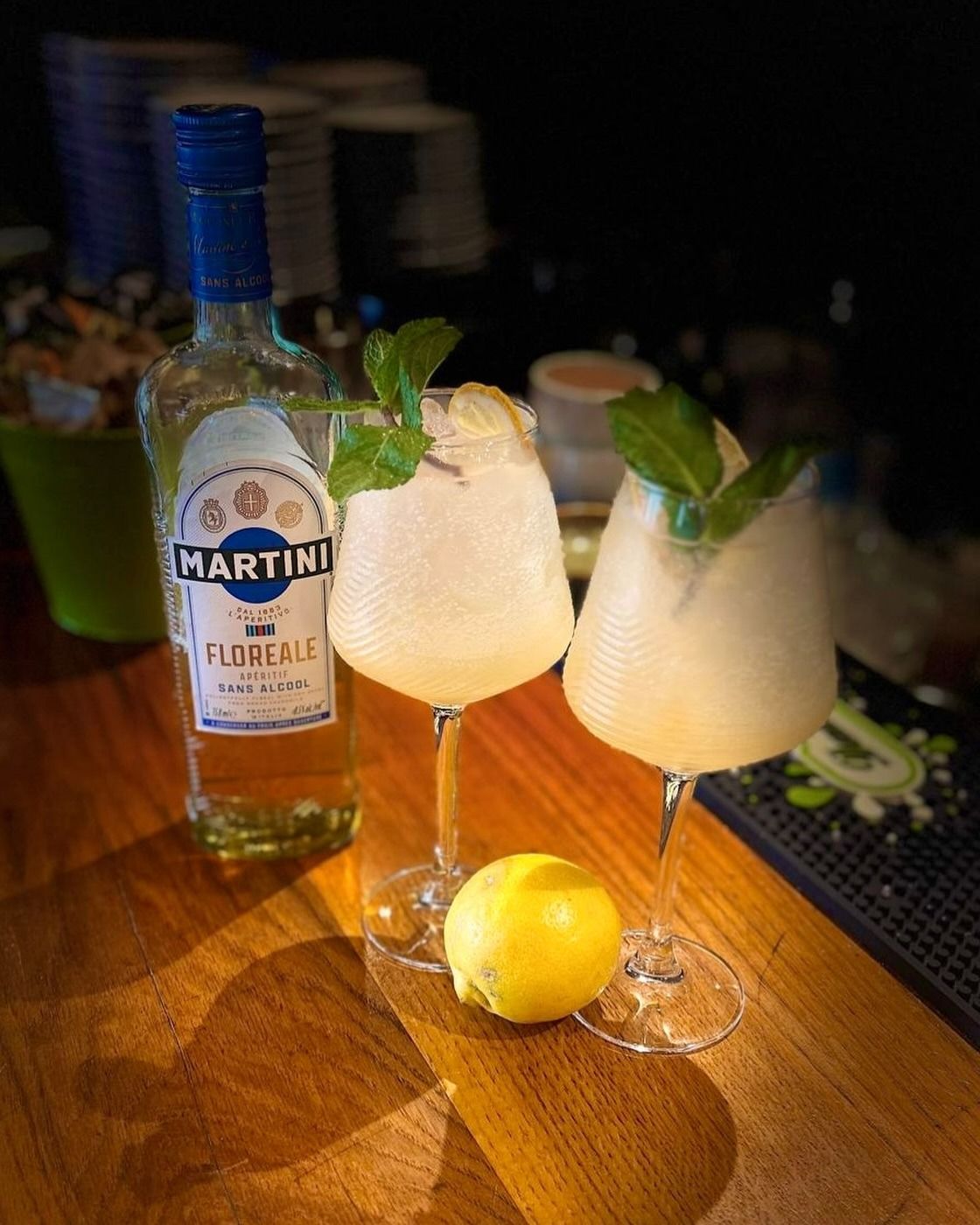Deux cocktails pâles à la menthe, une bouteille de Martini et un citron sur un comptoir de bar en bois
