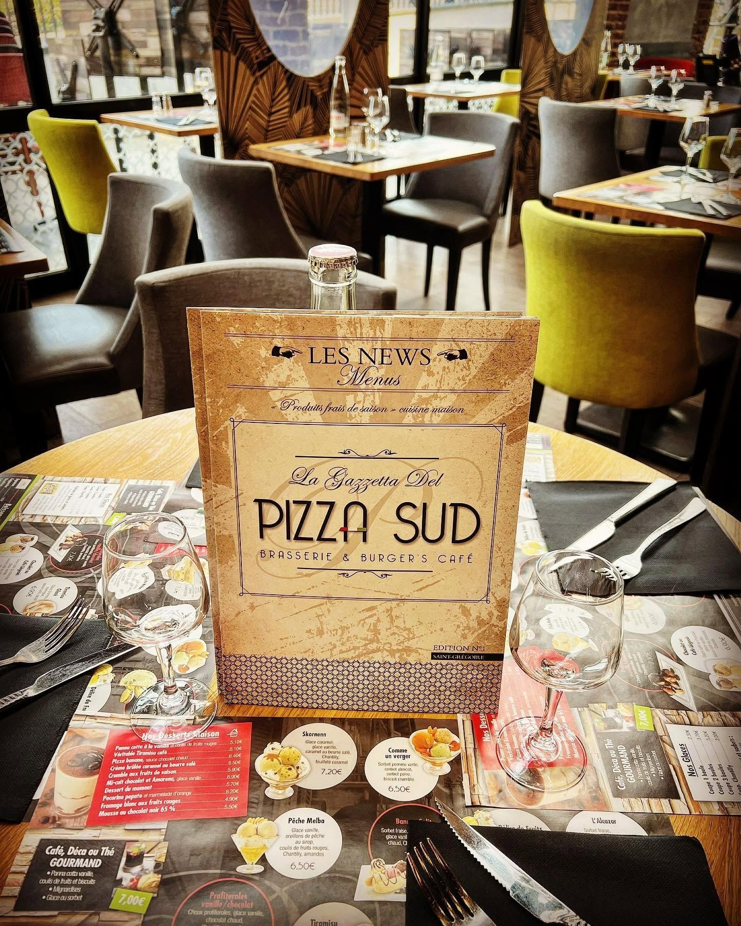 Table de restaurant avec un menu intitulé Pizza Sud, entourée de chaises et de sets de table