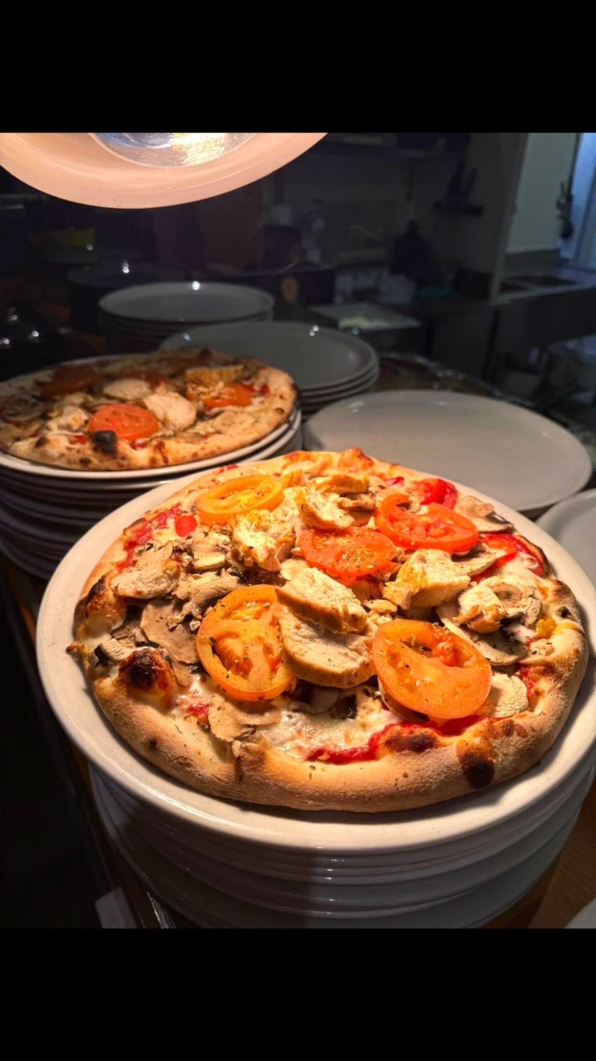 Des assiettes empilées de parts de pizza garnies de crevettes et de poivrons rouges, sous une lumière chaude de restaurant