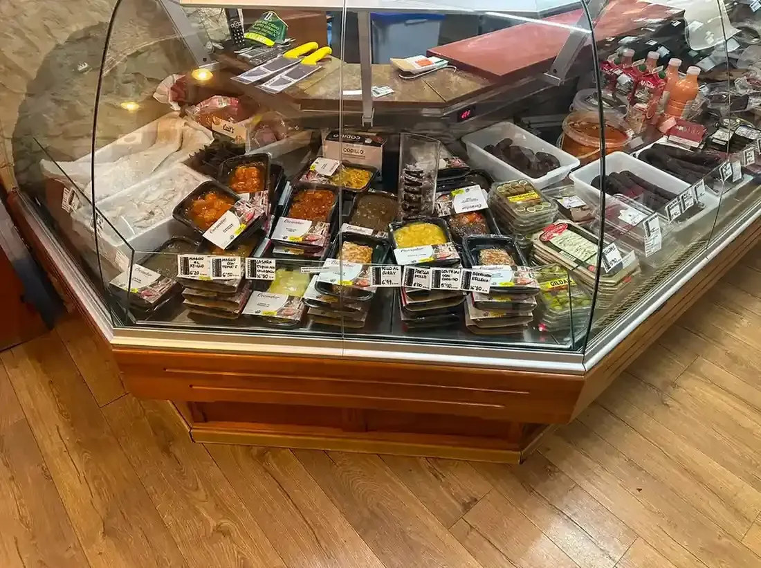 Vitrina de cristal de una pastelería llena de pasteles y tartas variadas sobre un suelo de madera.
