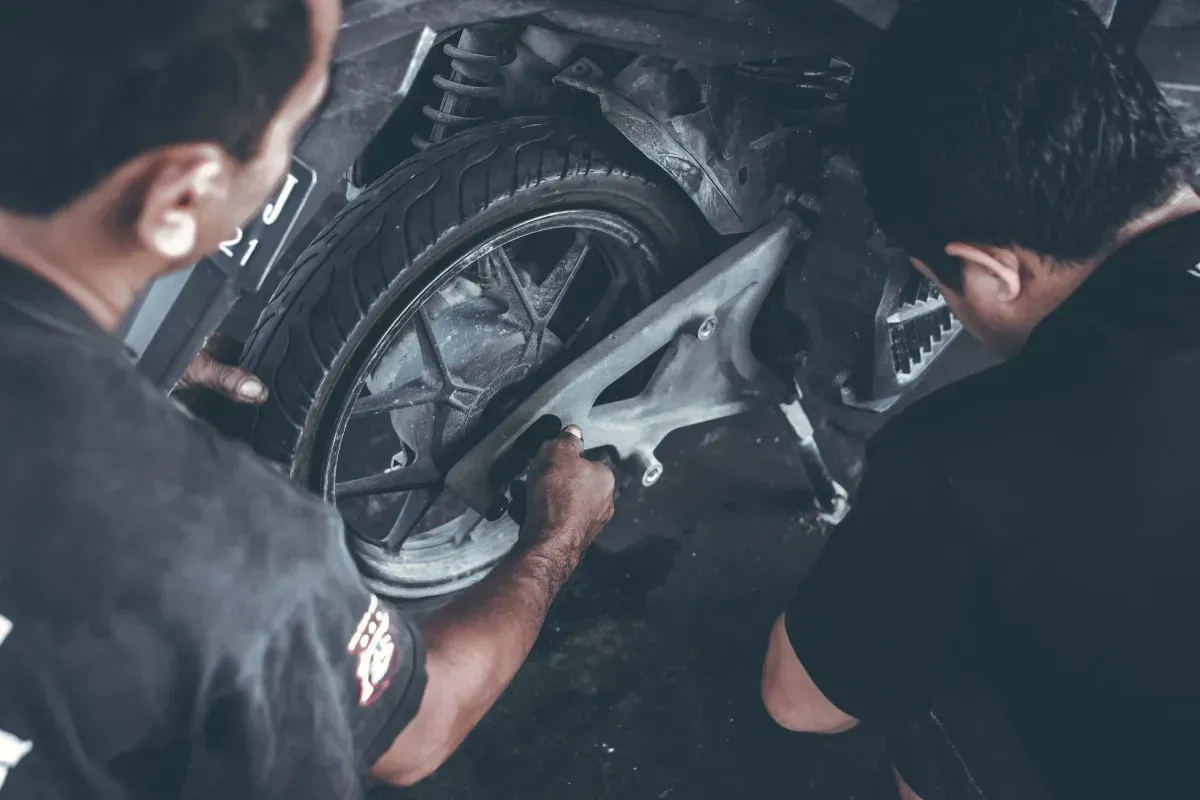 Dos mecánicos trabajando en un neumático de motocicleta; toma desde un ángulo bajo, manos visibles