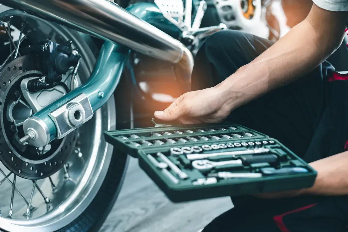 Persona trabajando en una motocicleta, sosteniendo una caja de herramientas.