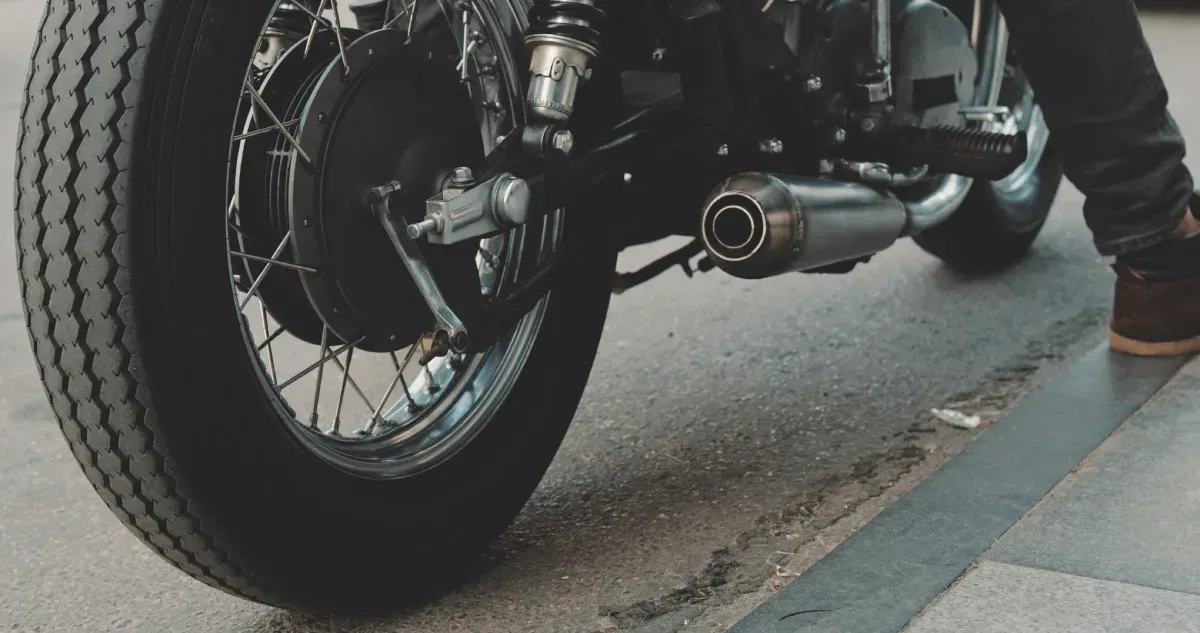 Primer plano del neumático trasero y del tubo de escape de una motocicleta negra en una calle pavimentada.