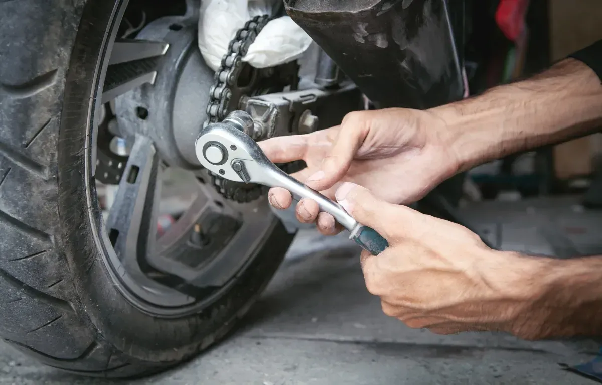 Persona que utiliza una llave para ajustar la cadena de una motocicleta en la rueda trasera.