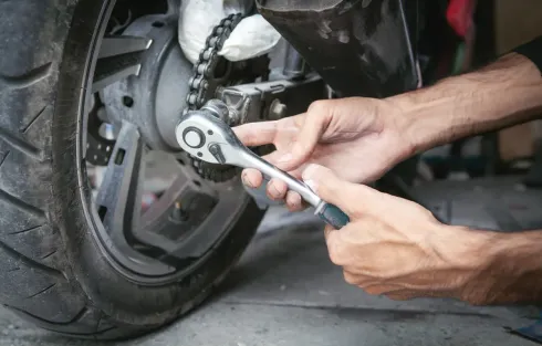 Persona que utiliza una llave para ajustar la cadena de una motocicleta en la rueda trasera.