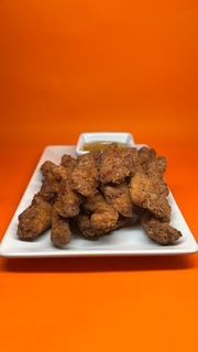 Tiras de pollo fritas en un plato blanco con salsa para mojar, sobre un fondo naranja.