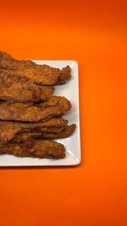 Tiras de comida frita en un plato blanco sobre un fondo naranja.