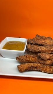 Tiras de pollo crujientes y salsa de mostaza en un plato blanco sobre un fondo naranja.