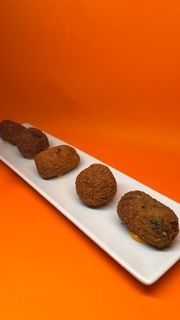 Cuatro alimentos fritos de color marrón dispuestos en un plato rectangular blanco sobre un fondo naranja.