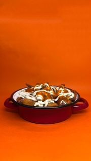 Plato de comida frita rociada con salsas blancas y rojas en un recipiente rojo sobre un fondo naranja.