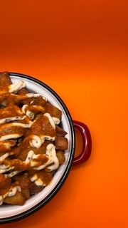 Papas fritas rociadas con salsa en un plato blanco y negro con un asa roja sobre un fondo naranja.