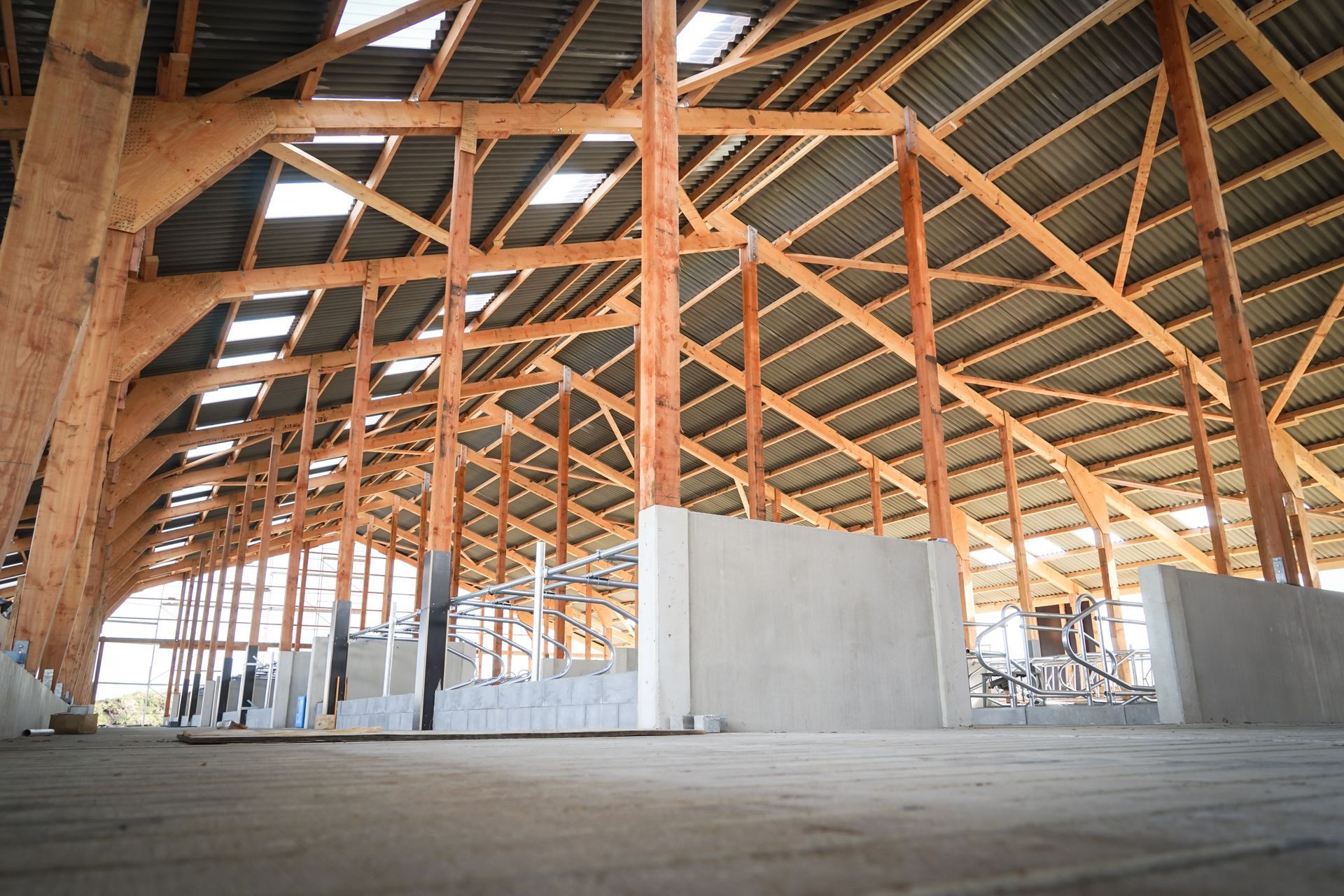 Innenraum einer großen Holzscheune mit hohen Bögen, Betonwänden und natürlichem Licht.