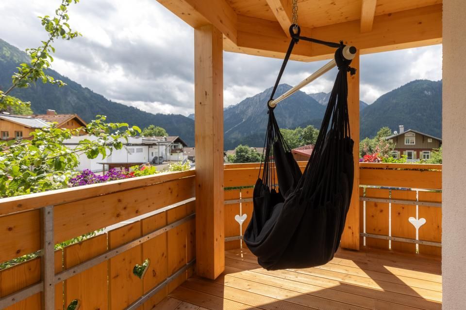 Eine schwarze Hängematte hängt von der Decke eines Balkons mit Bergen im Hintergrund.