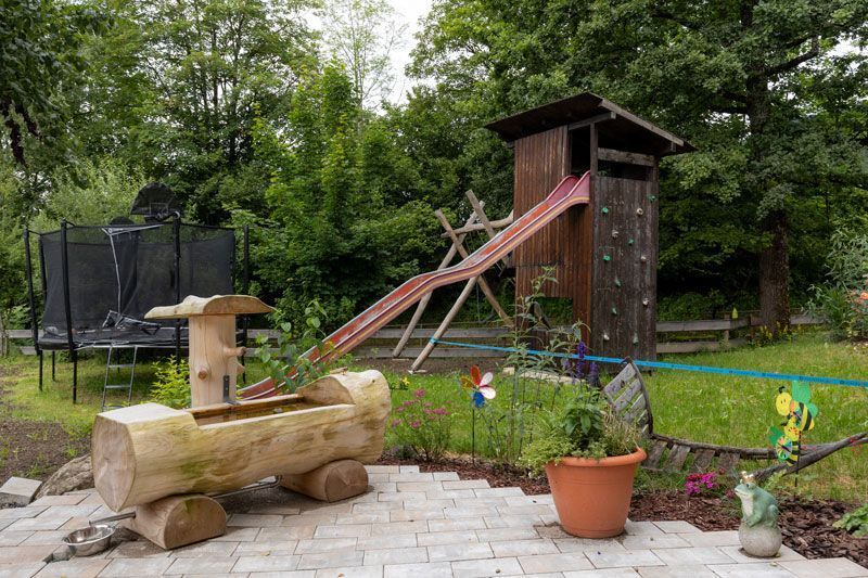 Ein Holzspielplatz mit Rutsche und Trampolin im Hinterhof.