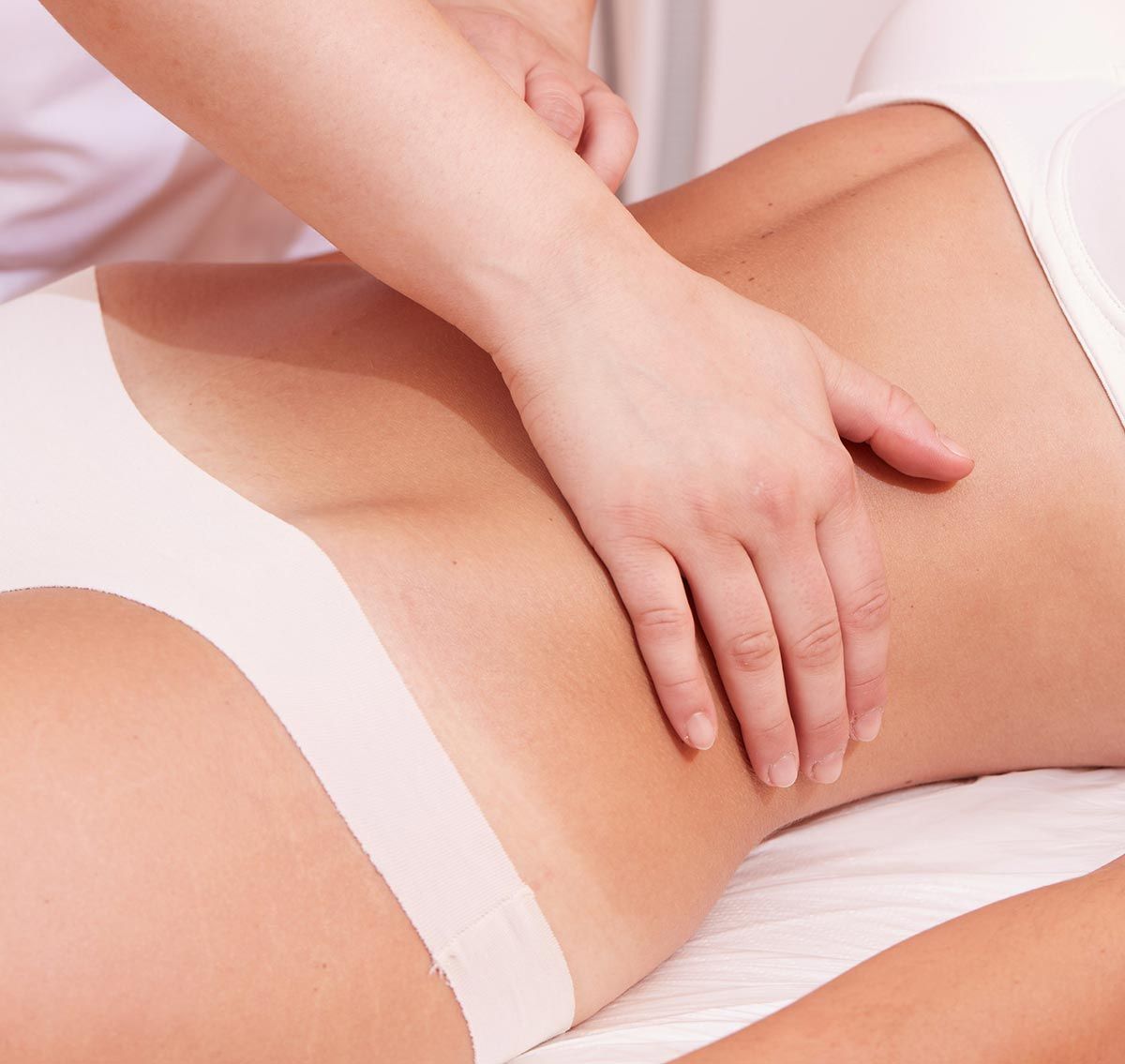 Manos masajeando el abdomen de una persona. La persona está acostada y viste ropa interior blanca.