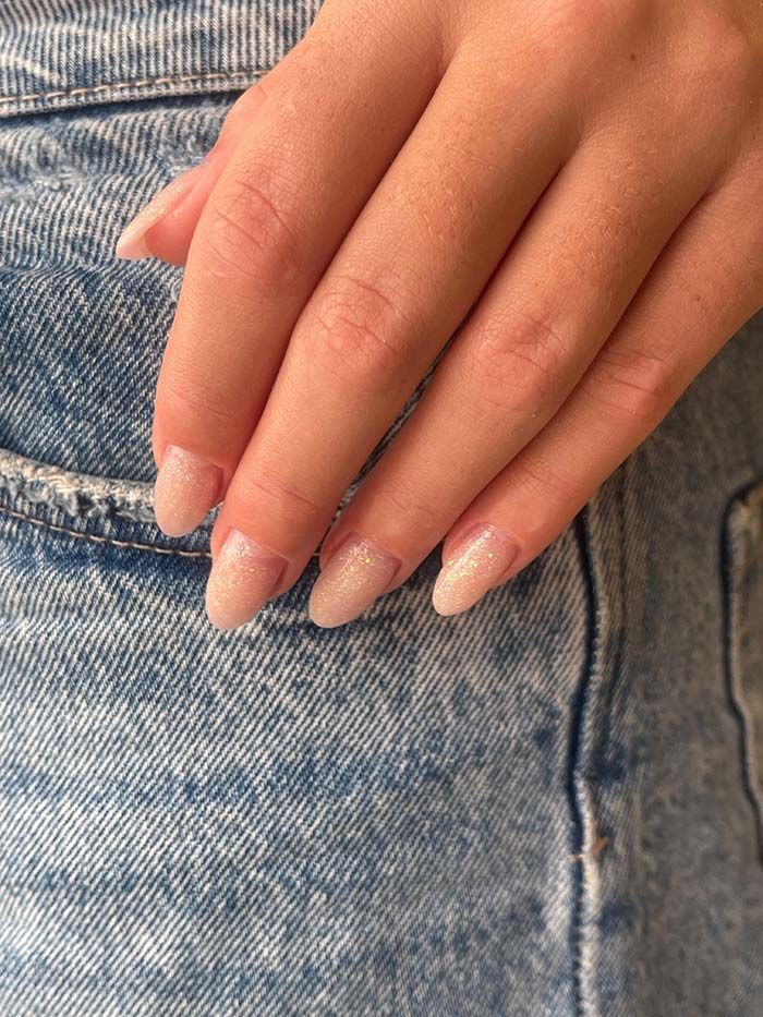 Mano con uñas ovaladas, pintadas con un esmalte rosa claro brillante, apoyada sobre unos vaqueros azules.