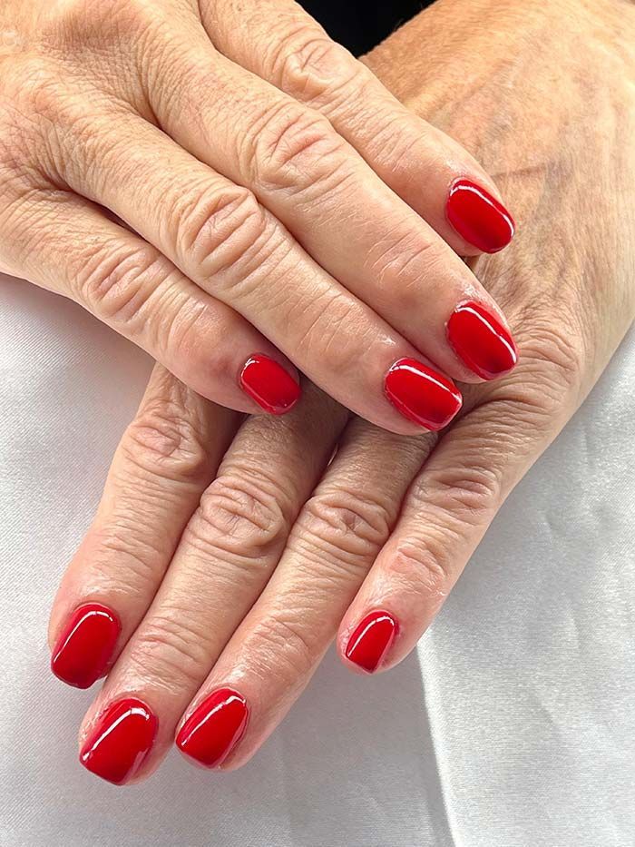 Manos con esmalte de uñas rojo, apoyadas sobre una superficie blanca.
