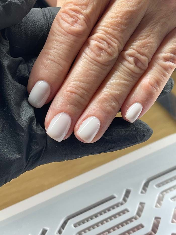 Mano con uñas cortas, de color rosa pálido y bien cuidadas, apoyada sobre un guante negro.