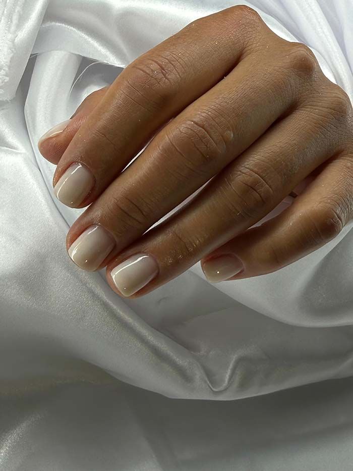 Mano con uñas cortas de tono neutro apoyada sobre tela blanca.