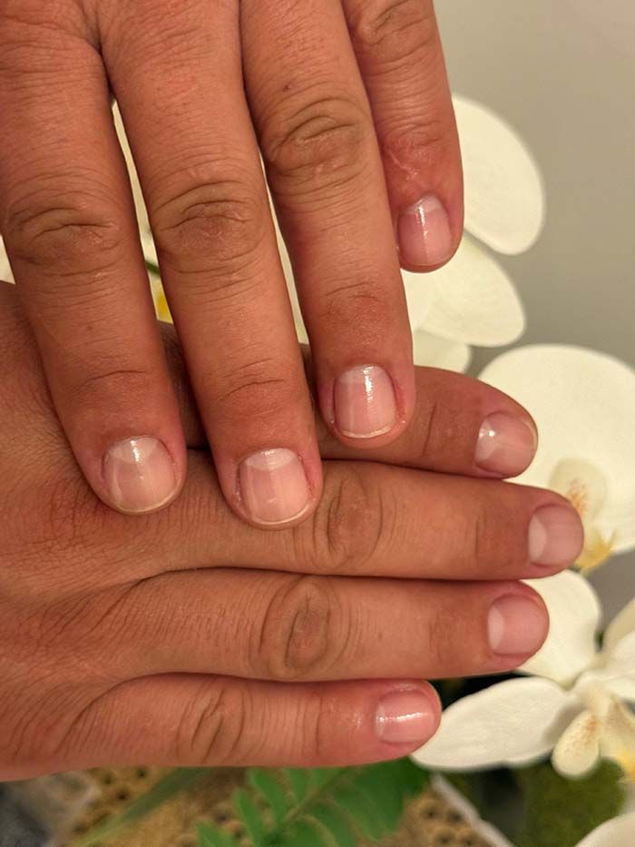 Manos con uñas cortas y bien cuidadas, mayormente con esmalte transparente y una sutil punta blanca.