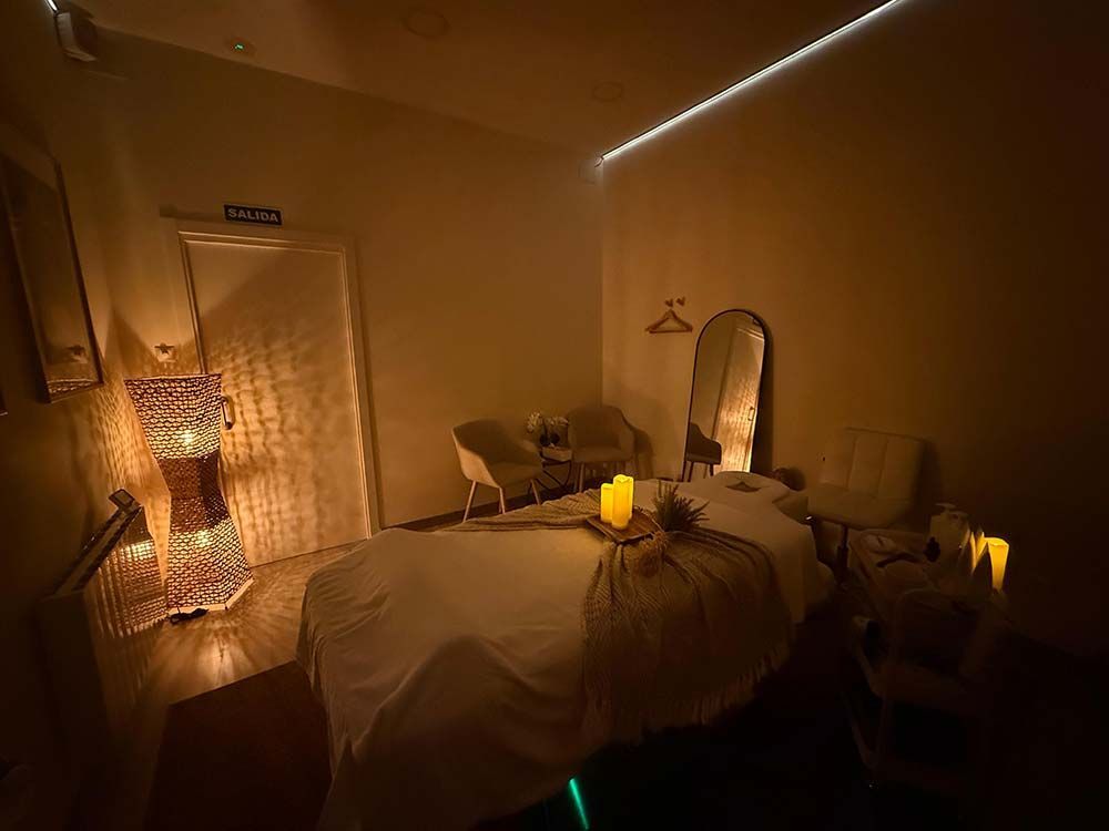 Habitación de spa con luz tenue, camilla de masaje, velas y espejos decorativos.