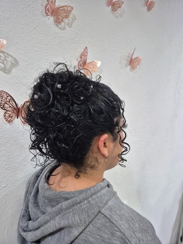 Una mujer con cabello rizado recogido en un moño está parada frente a una pared con mariposas en ella.