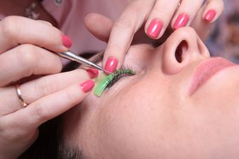 Una mujer con uñas rosas se está haciendo un maquillaje para las pestañas.