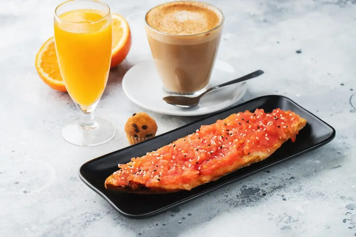 Desayuno: zumo de naranja, café con leche, tostadas con aderezo, panecillo pequeño y rodajas de naranja.