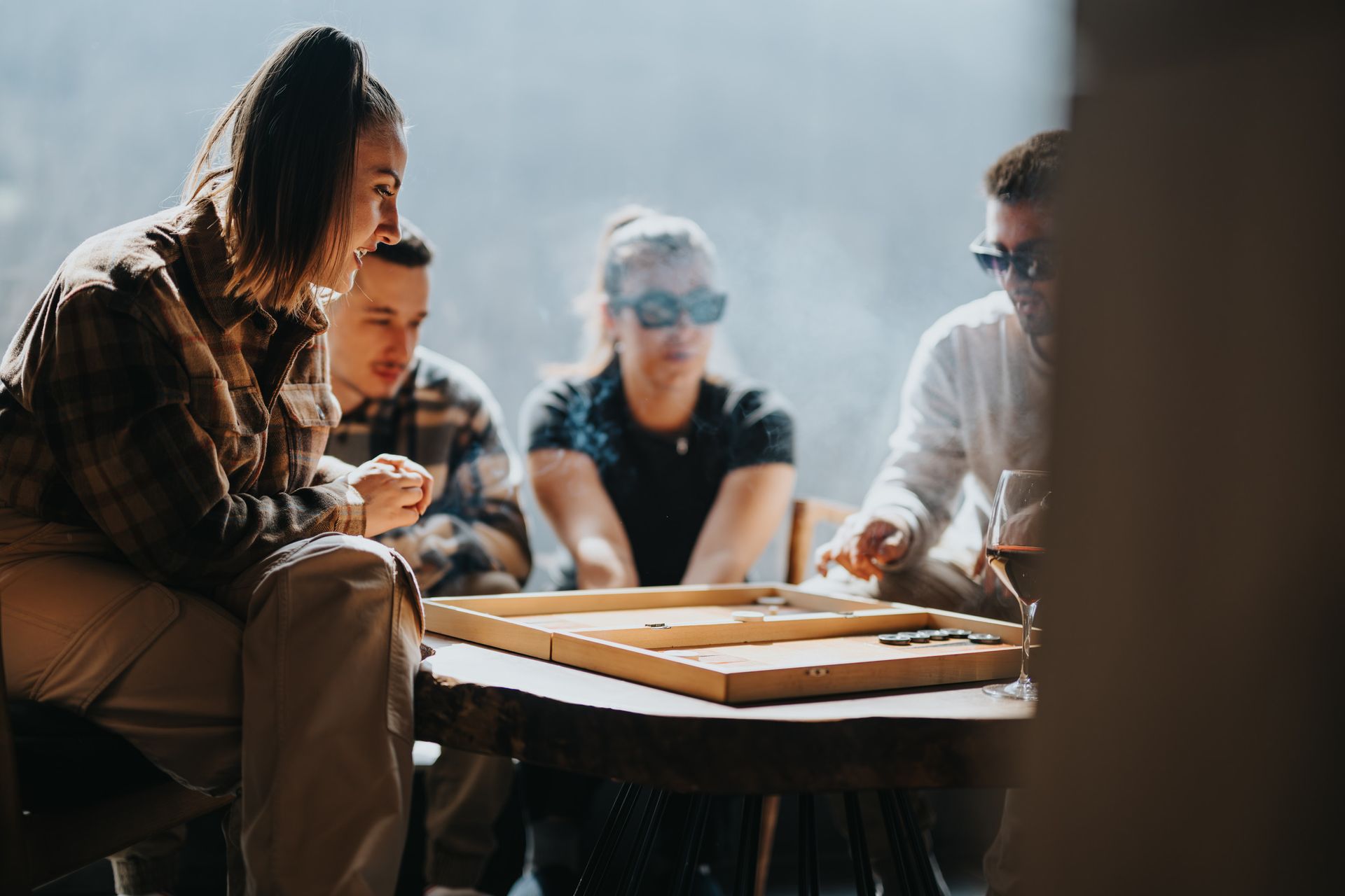 Cuatro personas jugando a un juego de mesa al aire libre; una con gafas de sol, los demás concentrados en el juego.