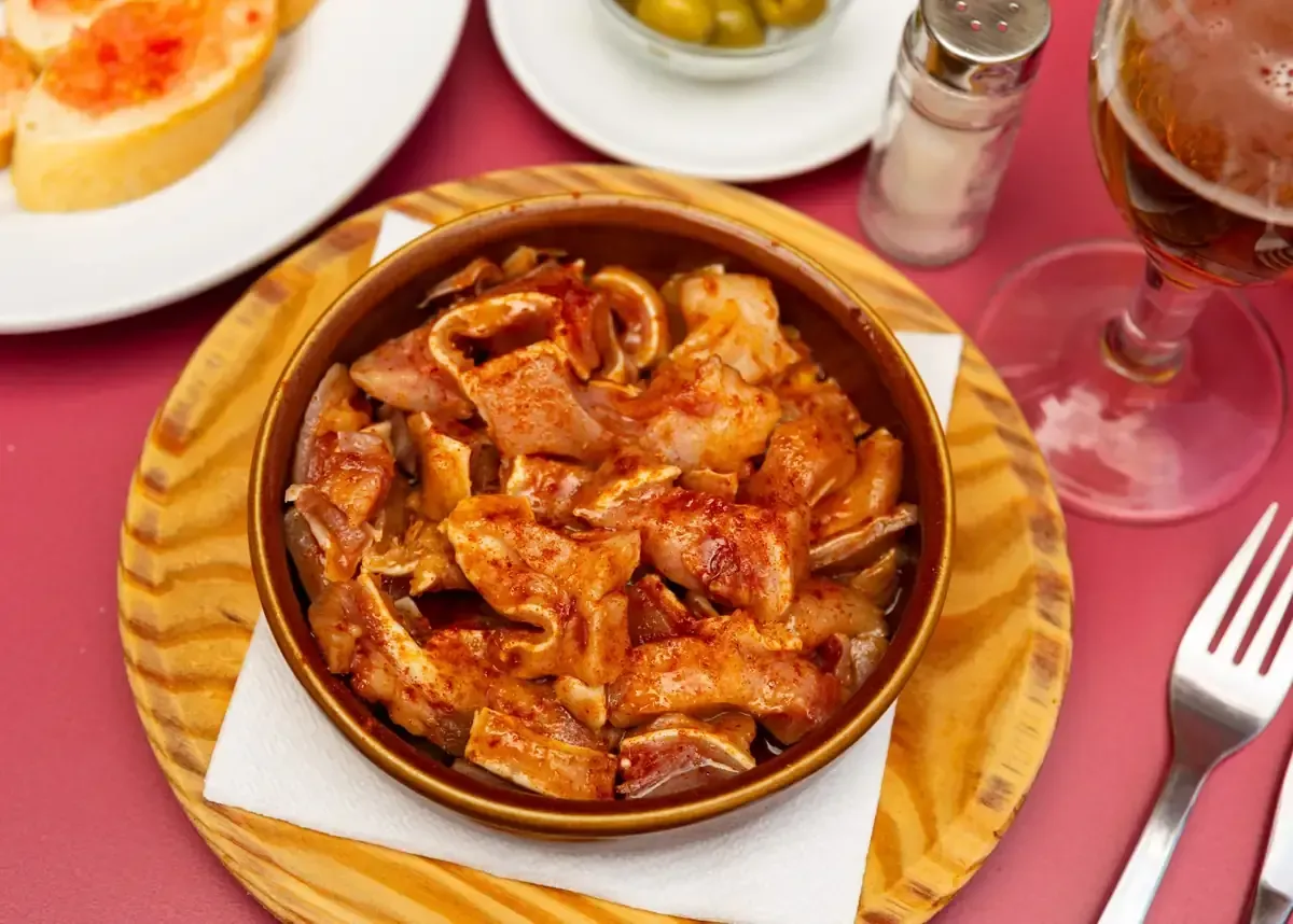 Plato de tapas de oreja de cerdo frita sazonada con pimentón, en un plato de madera, con pan, aceitunas y cerveza.