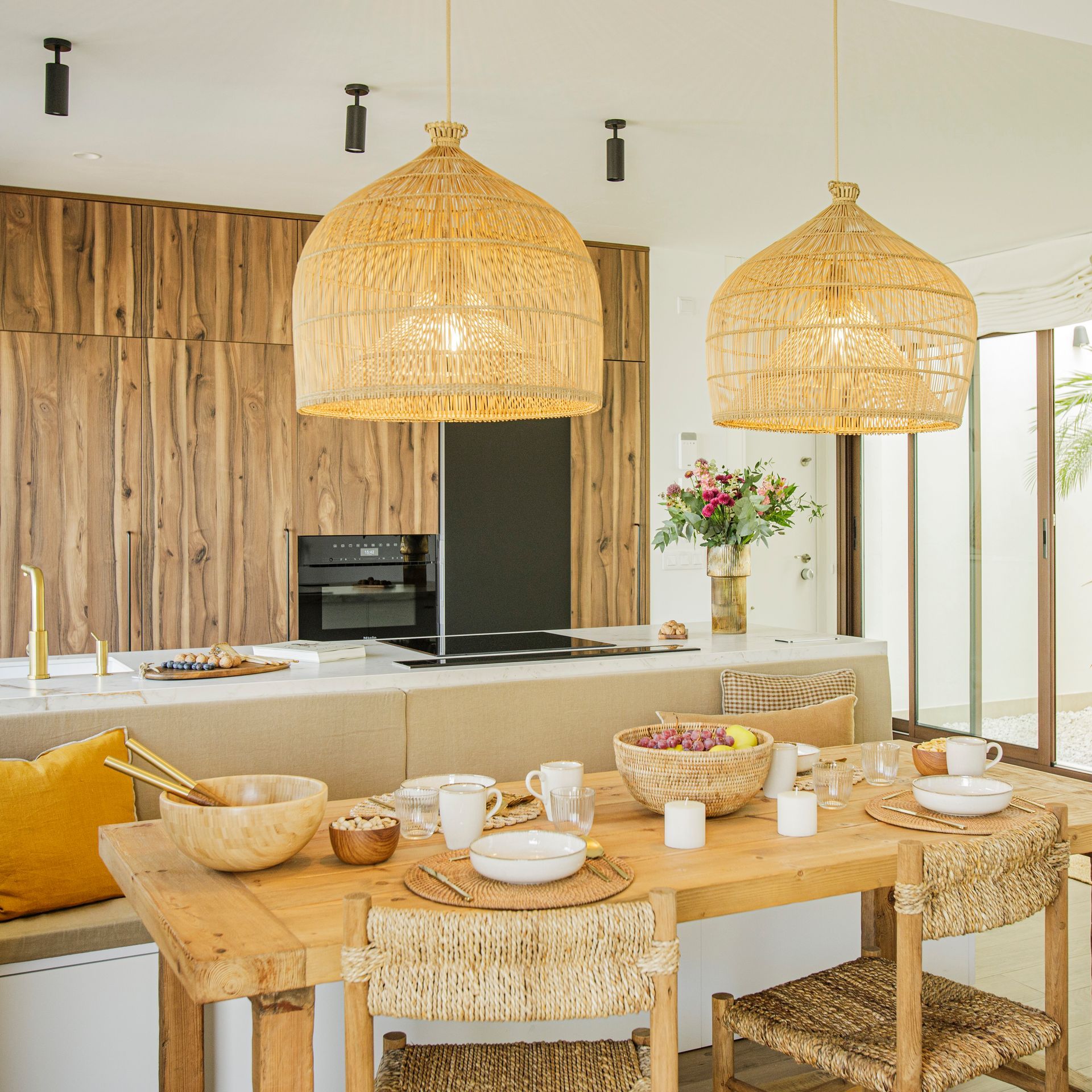 Comedor con sillas naranjas, mesa redonda y una lámpara colgante de colores. Cocina y estudio a la vista.