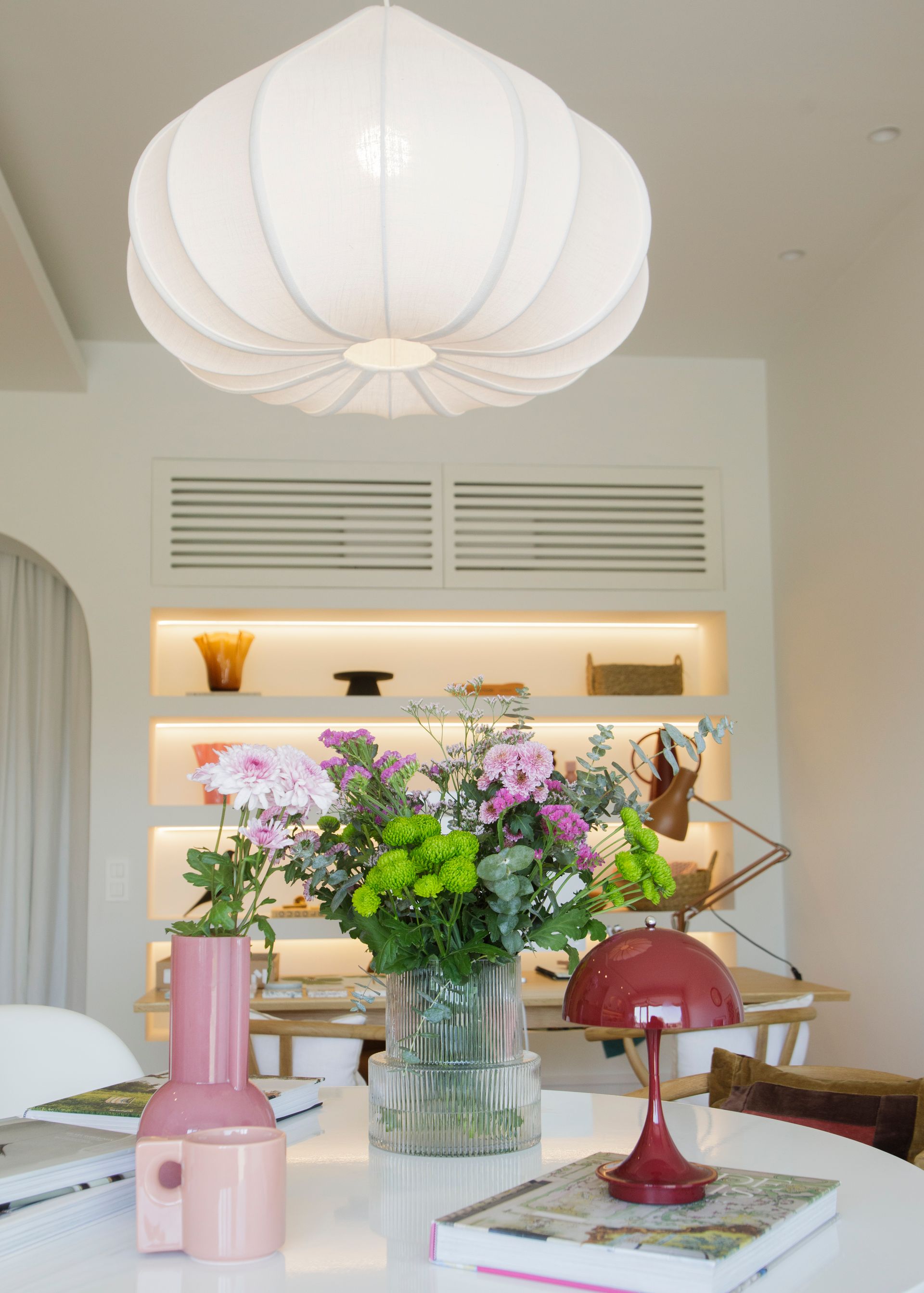 Interior de bar con taburetes, ventana circular y una pared de plantas.