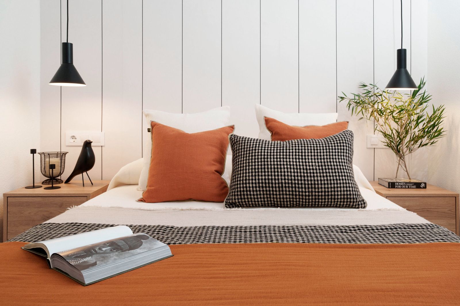 Dormitorio con cama, papel tapiz floral, cómoda de madera, planta grande y lámparas decorativas.