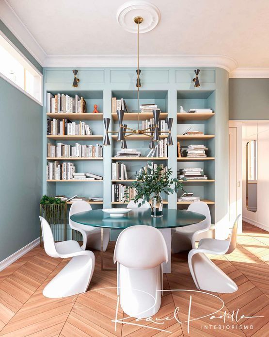 Comedor con mesa redonda de cristal, sillas blancas, estantería empotrada y paredes verde menta.