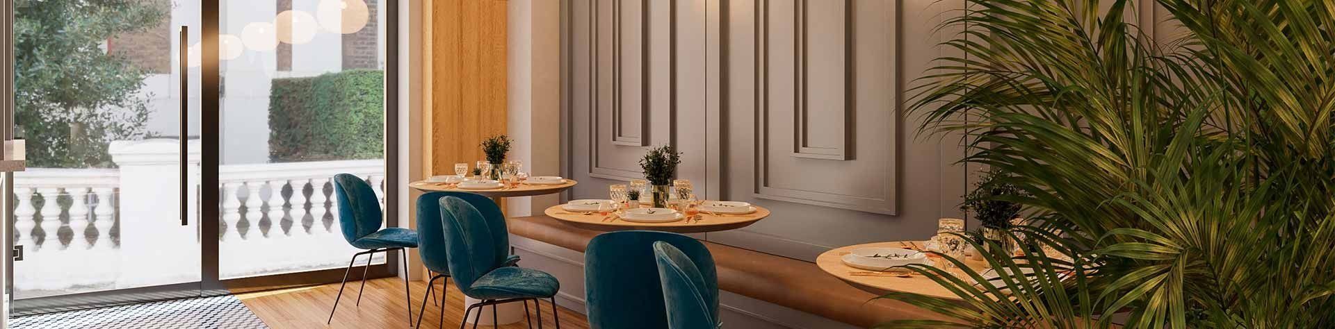 Interior de un restaurante con mesas redondas, sillas color verde azulado y una gran ventana con vista a la vegetación.