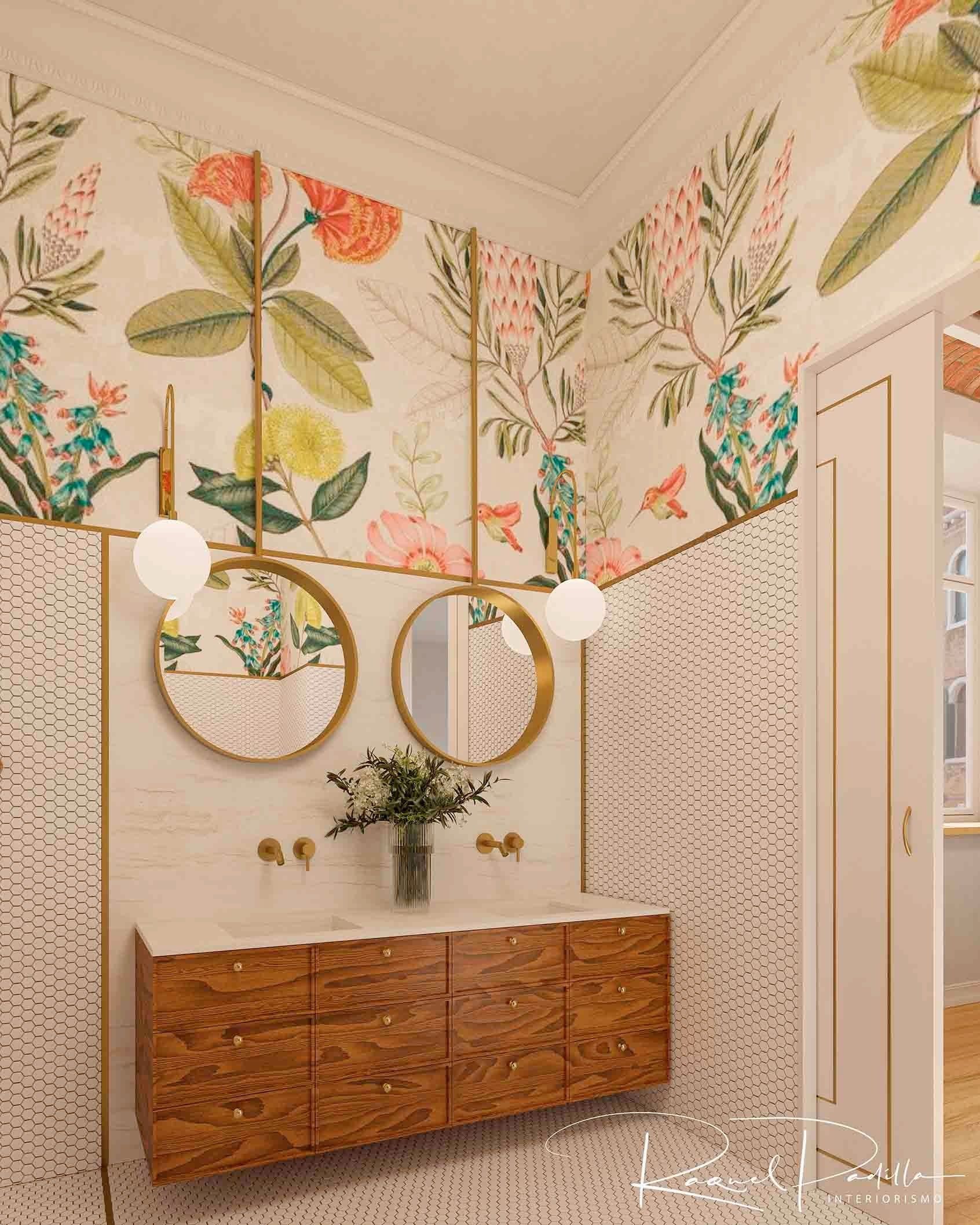 Baño con papel tapiz floral, detalles dorados, dos espejos redondos y un tocador de madera.