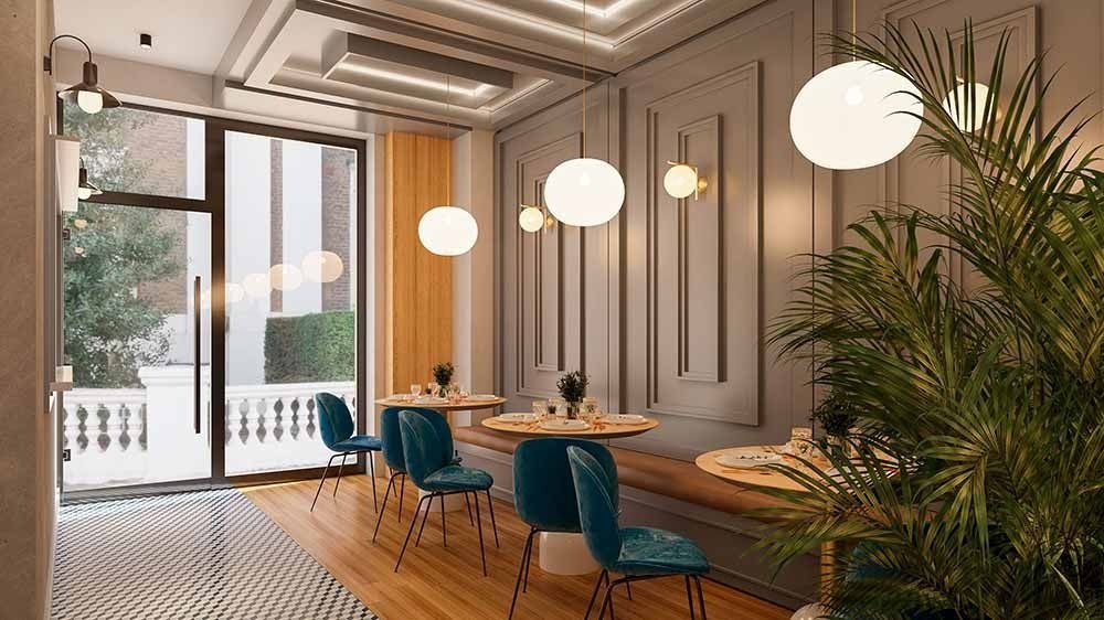 Interior de cafetería con mesas, sillas azules, luces de globo y plantas en macetas.