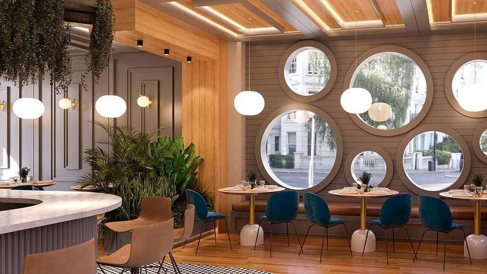 Interior de restaurante con ventanas redondas, sillas color verde azulado y luces colgantes.