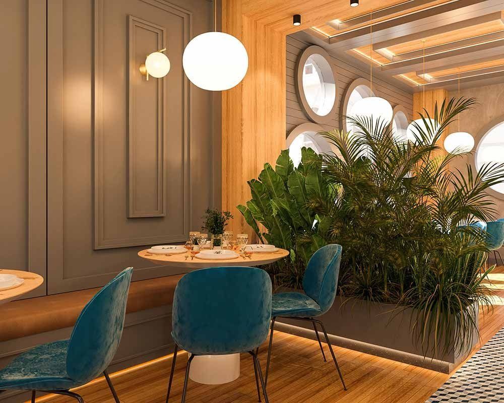 Interior de restaurante con sillas color verde azulado, mesas de madera, plantas y luces colgantes.
