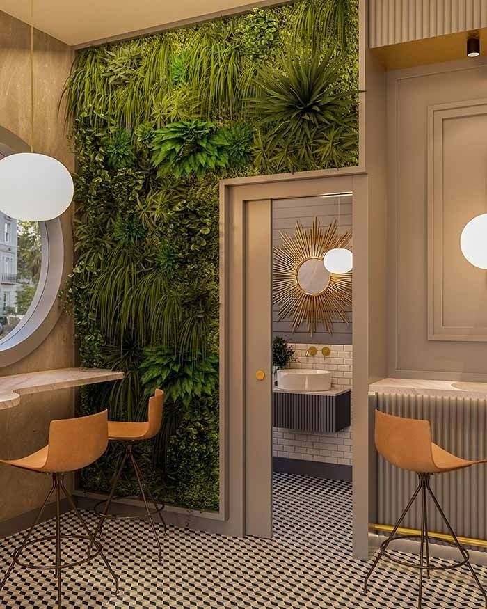 Interior de cafetería con una pared verde, dos taburetes de bar de color marrón y una puerta que conduce a un baño con un espejo decorativo y un lavabo.