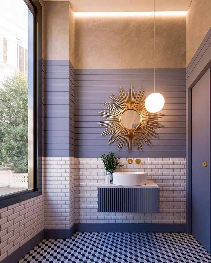 Baño con espejo dorado con efecto sol, paredes y suelos de azulejos azules y blancos, ventana.