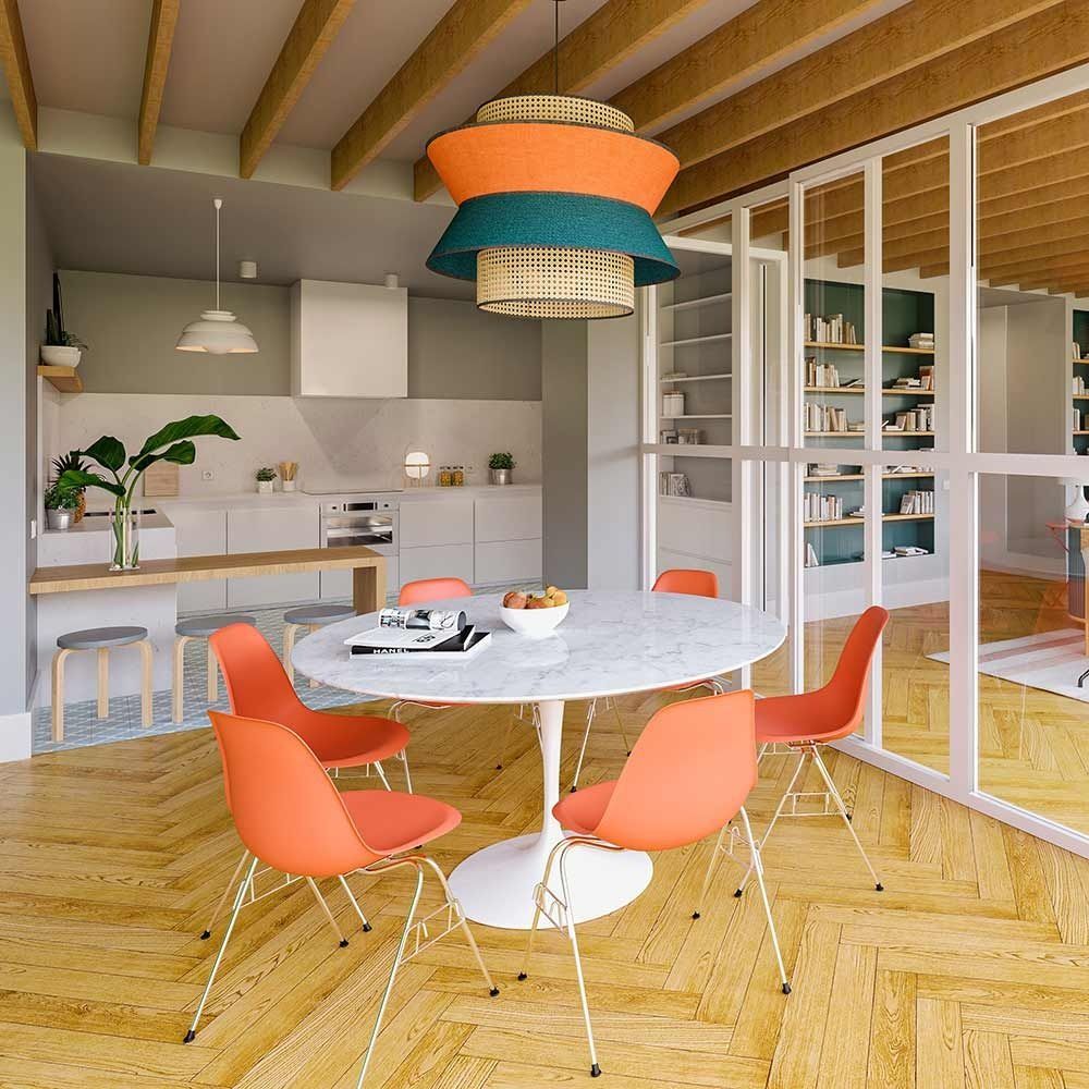 Comedor con sillas naranjas, mesa redonda y una lámpara colgante de colores. Cocina y estudio a la vista.