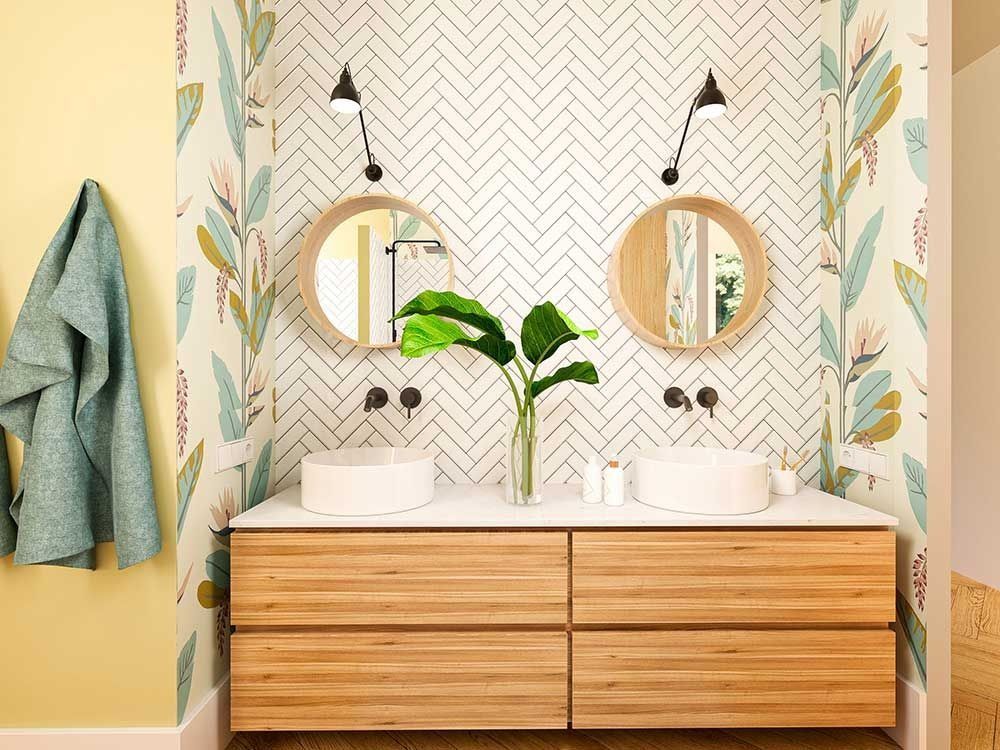Baño con tocador con dos lavabos, papel tapiz floral, espejos redondos e iluminación cenital.