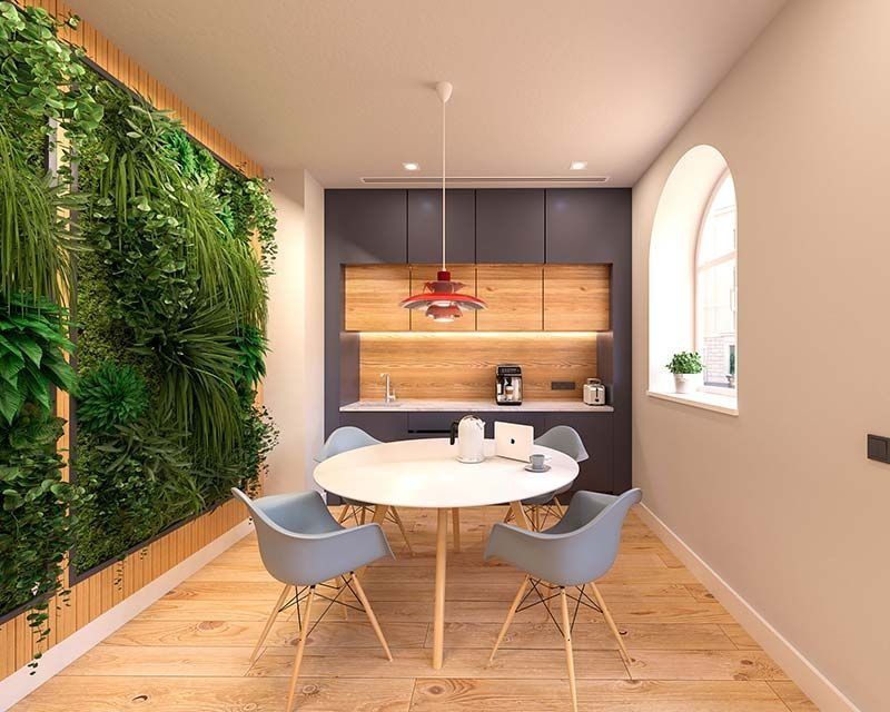 Moderno comedor con mesa redonda y sillas azules, junto a un muro de jardín vertical y una pequeña cocina.