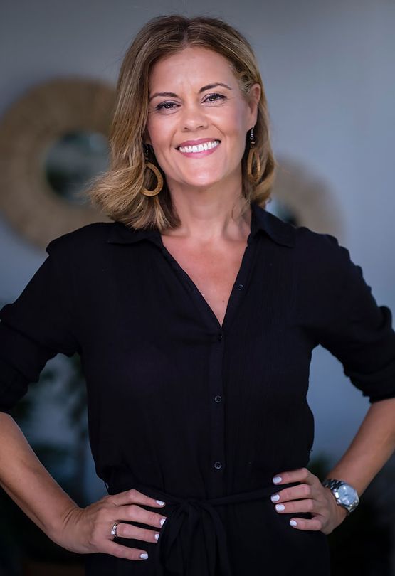 Mujer con camisa negra, manos en las caderas, sonriendo a la cámara.