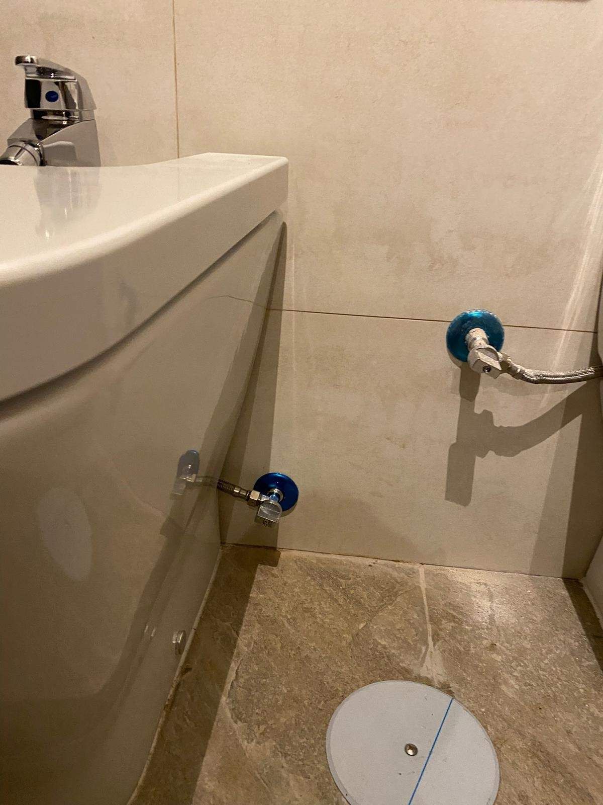 Bidé blanco con dos válvulas de agua azules en una pared de baño revestida de azulejos.