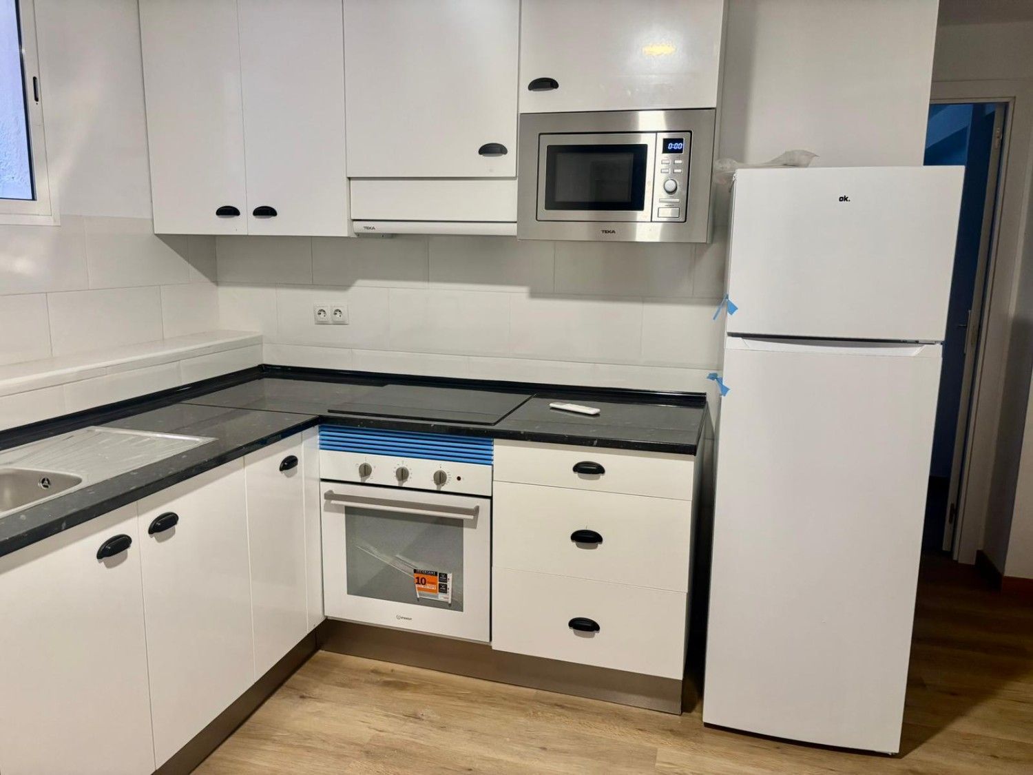 Gabinetes de cocina blancos, encimera negra, electrodomésticos de acero inoxidable y refrigerador.